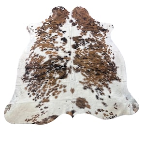 May include: A cowhide rug featuring a natural, irregular shape with a tri-color pattern of white, brown, and black patches. The hide displays a dense, short-haired texture with a central seam and organic, curved edges throughout the entire piece.