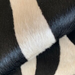 May include: Close-up of a black and white cowhide rug with a wavy pattern. The rug is made of soft, natural cowhide and has a luxurious feel.
