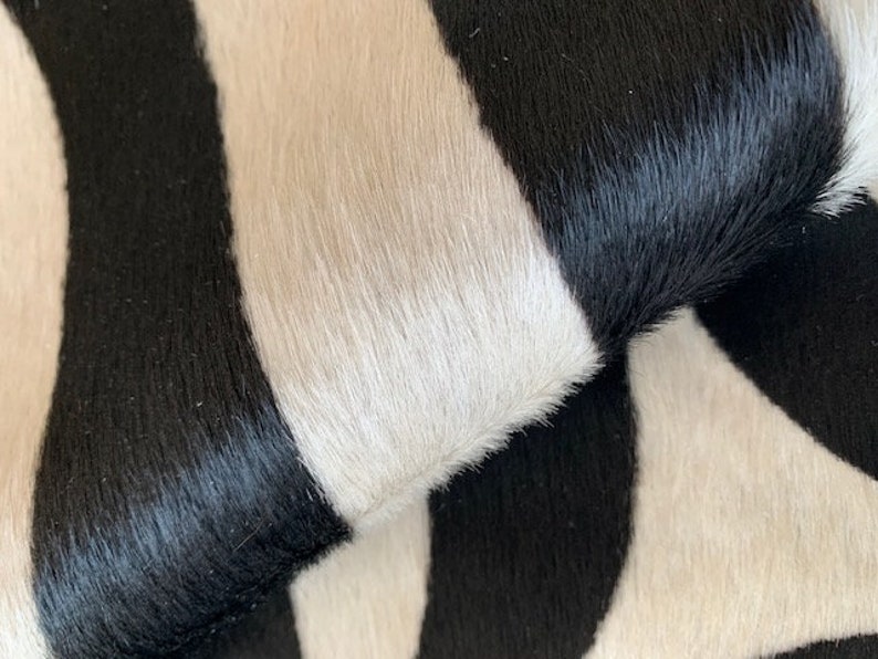 May include: Close-up of a black and white cowhide rug with a wavy pattern. The rug is made of soft, natural cowhide and has a luxurious feel.