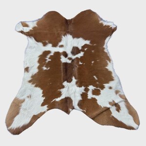 May include: A cowhide rug with a natural pattern of brown and white patches. The rug has an irregular shape, with the natural edges of the hide visible. The color palette is neutral, making it suitable for various interior design styles.