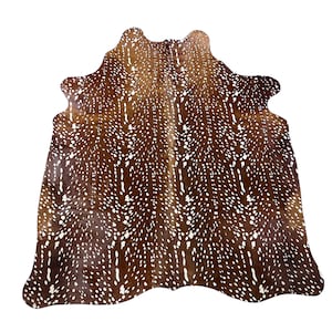 Puede incluir: Una alfombra de piel de vaca marrón y blanca con un patrón de manchas. La alfombra tiene una forma natural y está hecha de cuero genuino. La paleta de colores incluye tonos de marrón y blanco, creando un aspecto rústico y elegante. Esta alfombra es adecuada para la decoración del hogar.