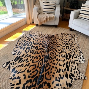May include: A brown and black leopard print cowhide rug with a natural, irregular shape. The rug is laid out on a light brown woven rug.
