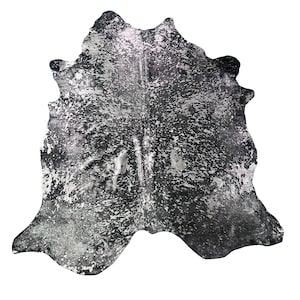 May include: A cowhide rug with a unique speckled pattern in shades of black, gray, and silver. The rug has an irregular shape, adding to its natural aesthetic. This decorative rug is suitable for living rooms and bedrooms.