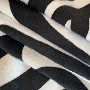 May include: Black and white cowhide rug with a striped pattern. The rug is made of soft, natural cowhide and has a unique, textured surface.