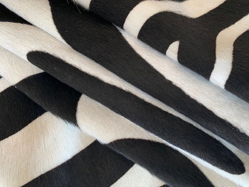 May include: Black and white cowhide rug with a striped pattern. The rug is made of soft, natural cowhide and has a unique, textured surface.
