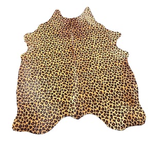 May include: An irregular, hide-shaped rug featuring a dense, repeating leopard print pattern. The design consists of small, dark brown and black rosettes scattered across a warm, golden-tan background, covering the entire surface area.