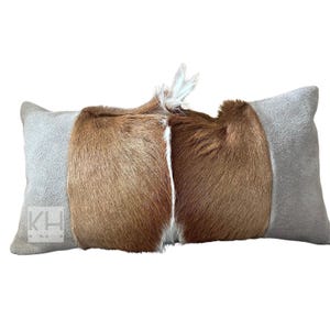 May include: A rectangular pillow with a brown and white cowhide pattern on the front and a light gray suede fabric on the back.