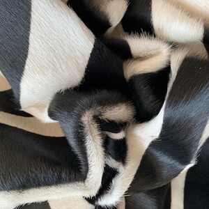 May include: Black and white cowhide rug with a striped pattern. The rug is made of soft, natural cowhide and has a luxurious feel.