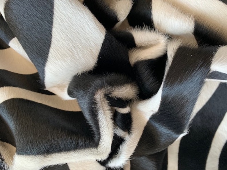 May include: Black and white cowhide rug with a striped pattern. The rug is made of soft, natural cowhide and has a luxurious feel.