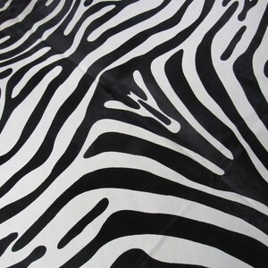 May include: Black and white zebra print fabric with a smooth, shiny texture.