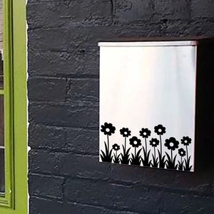 May include: A green door with a glass pane and a silver mailbox with a black flower design on the side of a brick building.