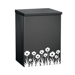 May include: A black metal mailbox with a white flower and grass design on the bottom.