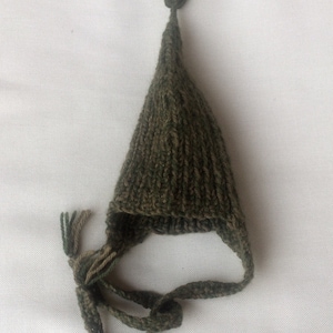 May include: A green knitted hat with a long pointed crown and a tassel on top. The hat has a long tie that can be tied under the chin.