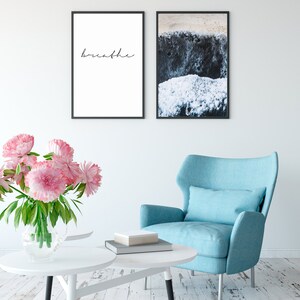 K&ouml;nnte beinhalten: Ein Wohnzimmer-Interieur mit einem blauen Sessel, einem wei&szlig;en Couchtisch und einem Strau&szlig; rosa Pfingstrosen in einer Glasvase. Zwei gerahmte Drucke h&auml;ngen an der Wand, einer mit dem Wort "breathe" und der andere mit einer Nahaufnahme einer Strandszene.