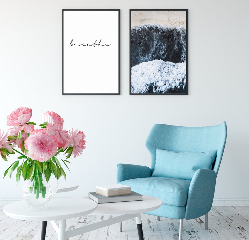 K&ouml;nnte beinhalten: Ein Wohnzimmer-Interieur mit einem blauen Sessel, einem wei&szlig;en Couchtisch und einem Strau&szlig; rosa Pfingstrosen in einer Glasvase. Zwei gerahmte Drucke h&auml;ngen an der Wand, einer mit dem Wort "breathe" und der andere mit einer Nahaufnahme einer Strandszene.