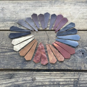 May include: A variety of leather strips in different colors and textures arranged in a circle on a wooden surface. The strips are all the same size and shape, and they are all cut to a point at one end.