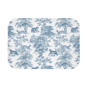 May include: A rectangular white bath mat with a blue toile pattern. The design features tigers, deer, and trees in a forest scene. The mat has rounded corners and a soft, absorbent texture.
