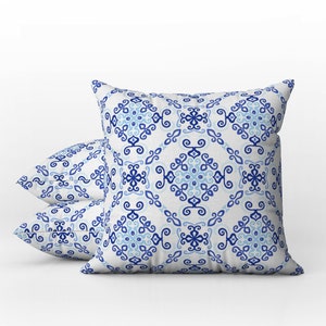 May include: Three square throw pillows with a white background and a repeating blue and light blue geometric pattern. The pillows are arranged in a stack, with one pillow in the foreground and two behind it.