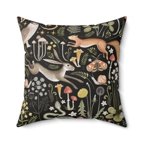 May include: Black throw pillow with a colorful illustration of a forest scene. The illustration features a rabbit, a squirrel, mushrooms, flowers, and a snail.