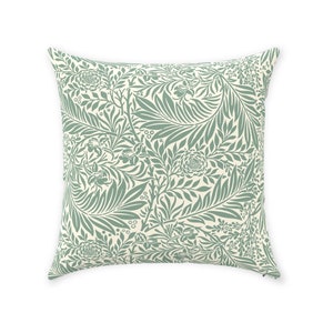 May include: A square throw pillow with a cream background and a green floral pattern. The pattern features stylized leaves and flowers.