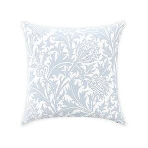 May include: A light blue throw pillow with a white floral pattern. The pattern features stylized leaves and flowers.