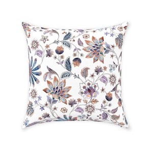 May include: A white throw pillow with a floral pattern in shades of blue, purple, and orange. The flowers are intricate and detailed, and the background is a soft white.
