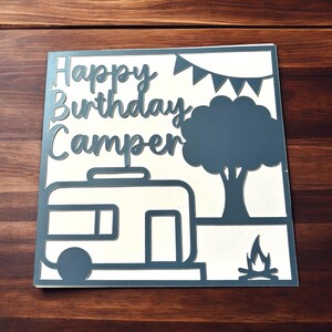 K&ouml;nnte beinhalten: Eine graue Karte mit dem Text "Happy Birthday Camper" auf wei&szlig;em Hintergrund. Die Karte zeigt einen Wohnwagen, einen Baum und ein Lagerfeuer.