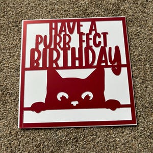 K&ouml;nnte beinhalten: Rote Karte mit wei&szlig;em Hintergrund und einer roten Katze, die &uuml;ber den Rand schaut. Die Karte sagt "Have a purrfect birthday".