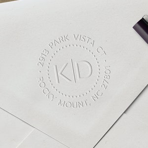 May include: A white envelope with a round, embossed return address stamp. The stamp reads "2913 Park Vista Ct. Rocky Mount, NC 27801" and has the initials "K.D." in the center.