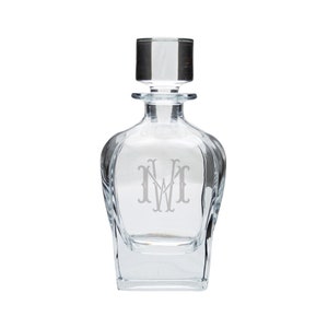 May include: A clear glass decanter with a square base and a stopper. The decanter is engraved with the monogram "N.W."