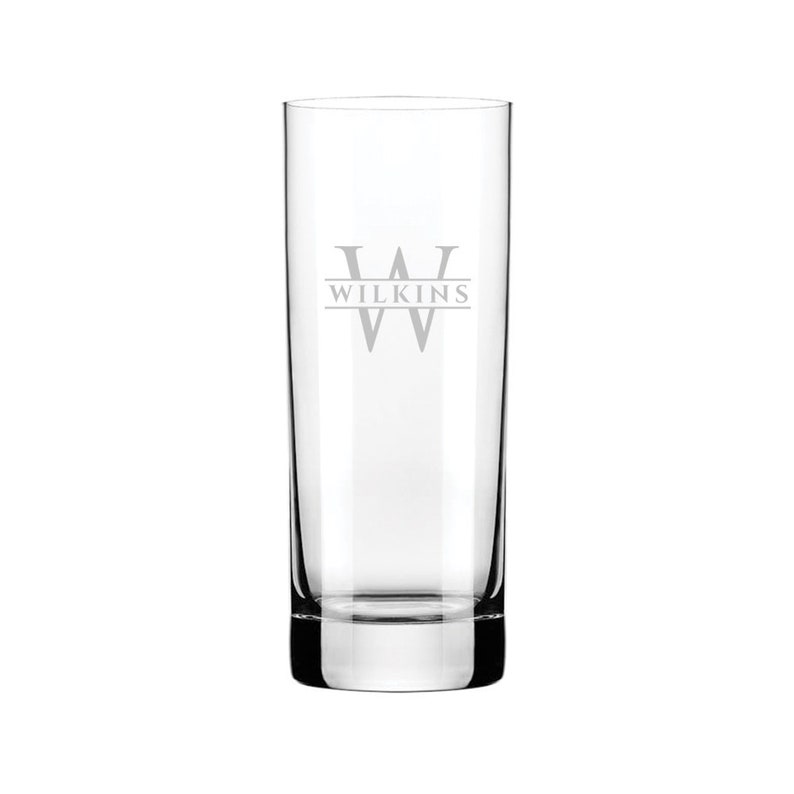 Puede incluir: Un vaso alto de vidrio transparente con un monograma personalizado. El vaso tiene una sola inicial "W" con el nombre "WILKINS" grabado debajo.