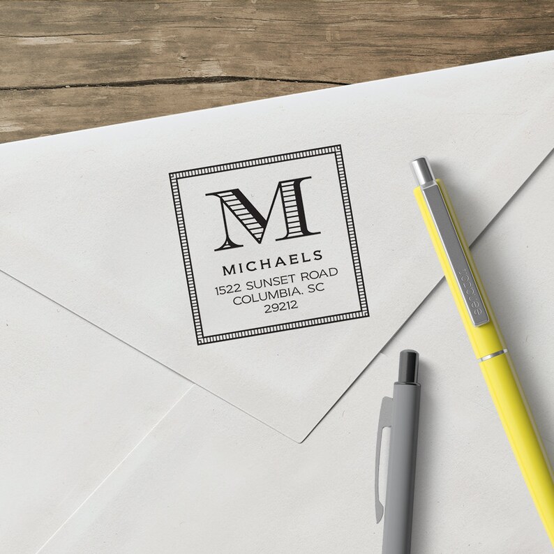 May include: A black and white return address stamp with a decorative border. The stamp features the letter "M" in a bold font with stripes and the text "Michaels, 1522 Sunset Road, Columbia, SC 29212".
