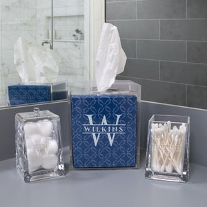 K&ouml;nnte beinhalten: Drei transparente Acryl-Badezimmer-Organizer mit einem blau-wei&szlig;en geometrischen Muster. Der Gewebeschachtel-Deckel tr&auml;gt den Namen "WILKINS" in wei&szlig;en Buchstaben. Der Wattebauschbeh&auml;lter und der Wattest&auml;bchenhalter haben ebenfalls den Namen "WILKINS" in wei&szlig;en Buchstaben.