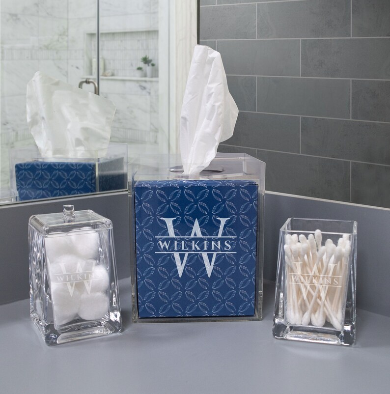 K&ouml;nnte beinhalten: Drei transparente Acryl-Badezimmer-Organizer mit einem blau-wei&szlig;en geometrischen Muster. Der Gewebeschachtel-Deckel tr&auml;gt den Namen "WILKINS" in wei&szlig;en Buchstaben. Der Wattebauschbeh&auml;lter und der Wattest&auml;bchenhalter haben ebenfalls den Namen "WILKINS" in wei&szlig;en Buchstaben.