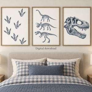 May include: Three framed wall art prints featuring blue watercolor dinosaur illustrations on a white background. The left print shows dinosaur footprints, the center print displays three full dinosaur skeletons, and the right print shows a large skull.