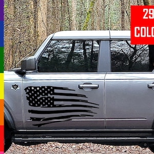 May include: A gray Ford Bronco with a black distressed American flag decal on the driver's side door. The decal is a popular choice for car enthusiasts and patriotic individuals. 29+ Colors.