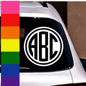 May include: A black and white monogram decal with the letters ABC in a circle. The decal is on the back window of a white car.