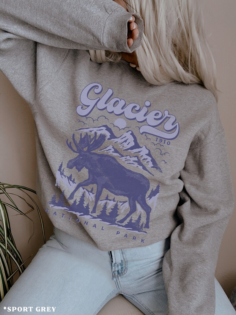 May include: A gray sweatshirt with a purple graphic of a moose standing in front of mountains with the text "Glacier National Park 1910" printed on it.