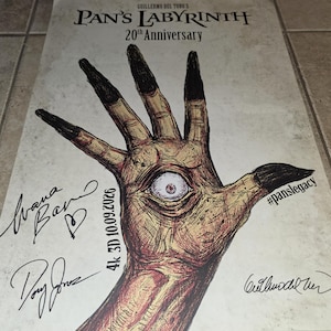 May include: A Pan's Labyrinth 20th Anniversary poster featuring a detailed illustration of a hand with an eye in the palm and long black fingernails. The poster includes the text Guillermo del Toro's Pan's Labyrinth, 4k 3D 10.09.2026, and #panslegacy, along with several handwritten signatures.