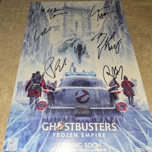May include: A movie poster for the film "Ghostbusters: Frozen Empire" featuring a white Ecto-1 car with a Ghostbusters logo on the front. The poster has a blue and white icy background with the text "Coming Soon" at the bottom.