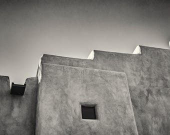 May include: A black and white photograph of a building with a single window. The building is constructed from concrete and has a rough texture. The window is small and rectangular, and it is set into the wall.
