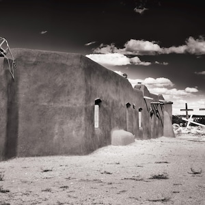 Könnte beinhalten: Ein Schwarzweißfoto eines verwitterten Adobe-Gebäudes mit rustikalem Südwest-Flair. Das Gebäude hat mehrere Fenster und ein Flachdach. Das Gebäude steht vor dem Hintergrund eines bewölkten Himmels.