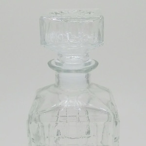 May include: A clear glass decanter with a square body and a square stopper. The decanter has a textured, checkered pattern.
