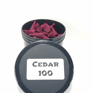 May include: A black container with a white label that says "CEDAR 100". The container is filled with red incense cones.