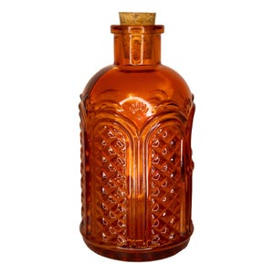 May include: An amber-colored glass bottle with a cork stopper. The bottle has a decorative, diamond-patterned design and a rounded shape. The bottle is likely used for storing liquids and has a vintage aesthetic.