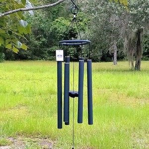 May include: A dark blue wind chime suspended from a tree branch. The chime features a circular top, multiple cylindrical tubes, and a circular wind catcher. The background shows green grass and trees.