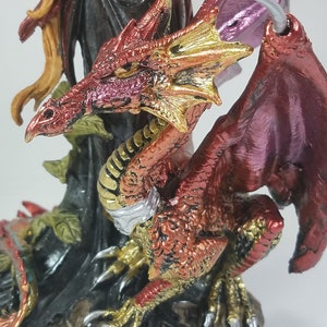 May include: A red and gold dragon figurine with wings outstretched. The dragon has a detailed, textured surface and is perched on a base with a leafy design.