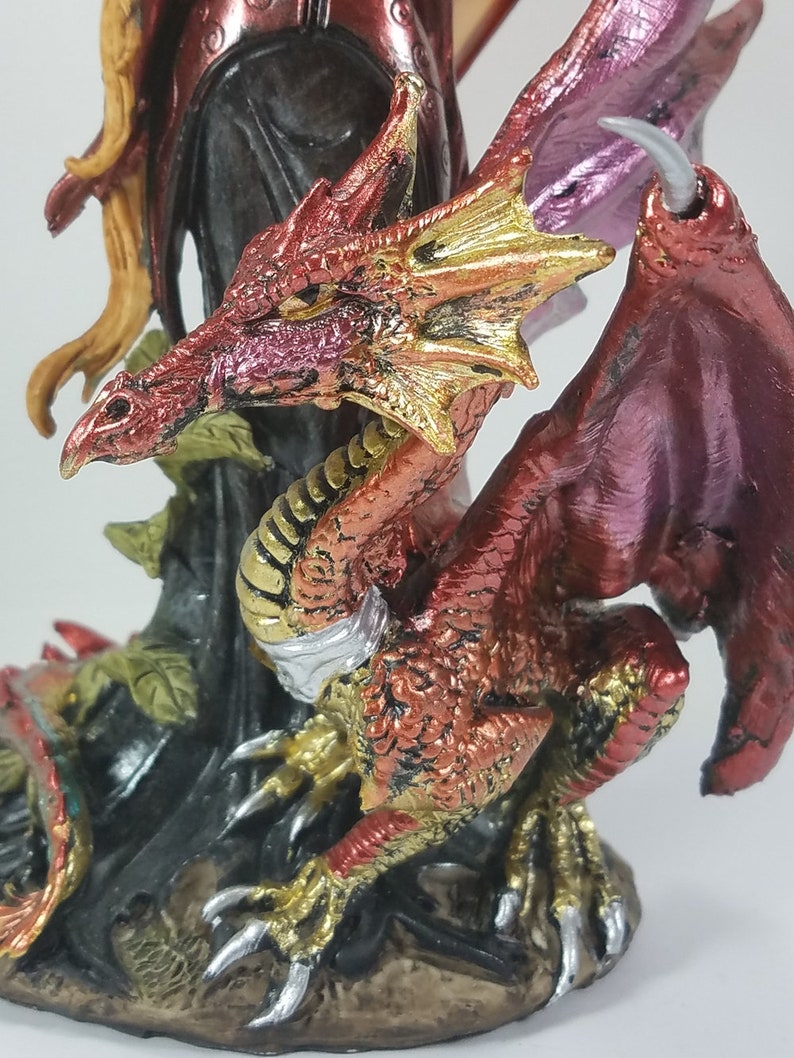 May include: A red and gold dragon figurine with wings outstretched. The dragon has a detailed, textured surface and is perched on a base with a leafy design.