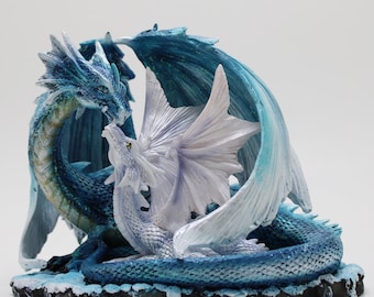 Può includere: Una statuetta fantasy di due draghi, uno blu e uno bianco, intrecciati. Il drago blu ha scaglie iridescenti e ali spiegate. Il drago bianco ha grandi ali aperte. La base è una superficie scura e strutturata con accenti ghiacciati.