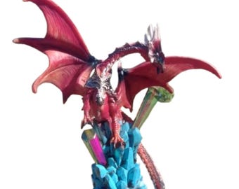 Può includere: Una statuetta di drago rosso appollaiata su una formazione di cristallo blu. Il drago ha le ali spiegate e una lunga coda. La base di cristallo è dettagliata con accenti iridescenti.